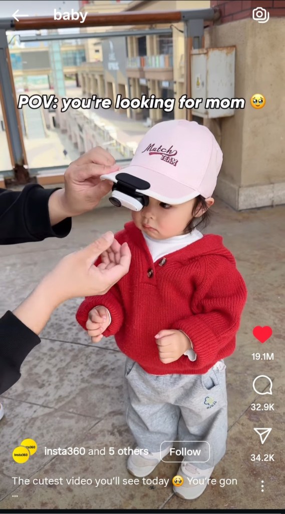 A baby wearing a pink cap with a camera attached is being assisted by an adult, looking around curiously. Text overlay reads, 'POV: you're looking for mom.'